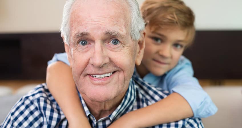Happy elderly man with grandson embracing for a photo.