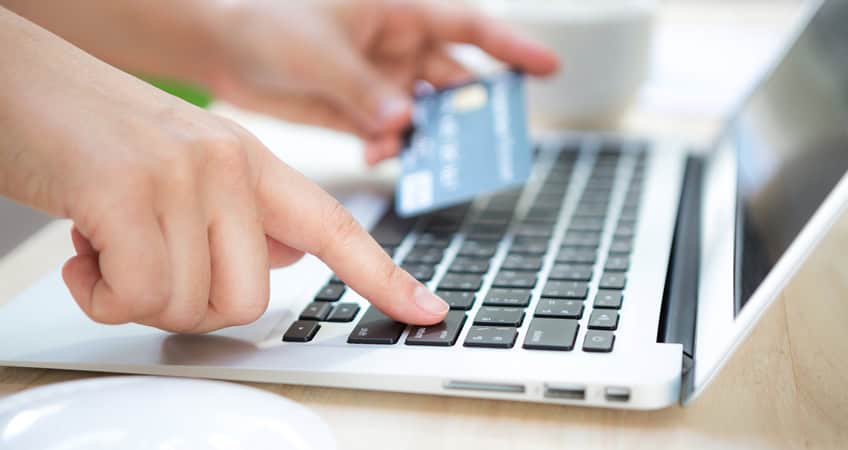 A senior citizen using a credit card on a laptop for online activities.