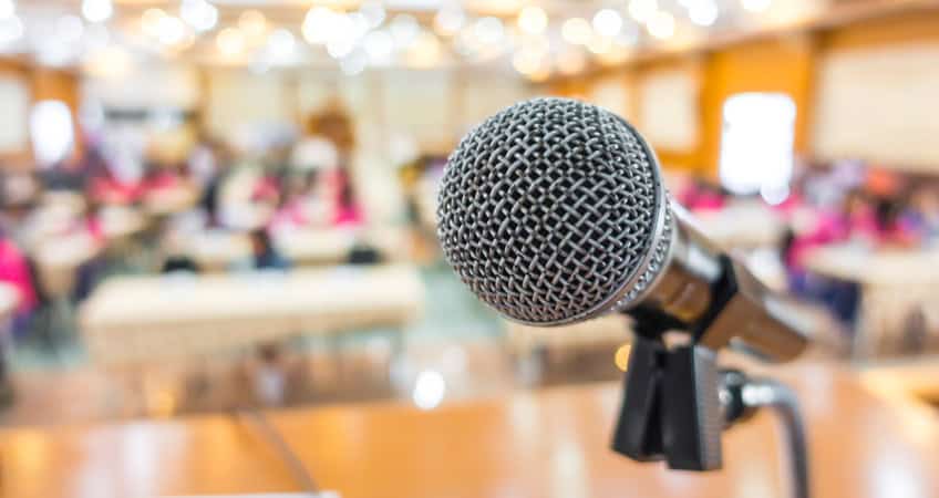 Alt text: Microphone at Irish Senior Citizens Parliament, with a blurred audience in background.