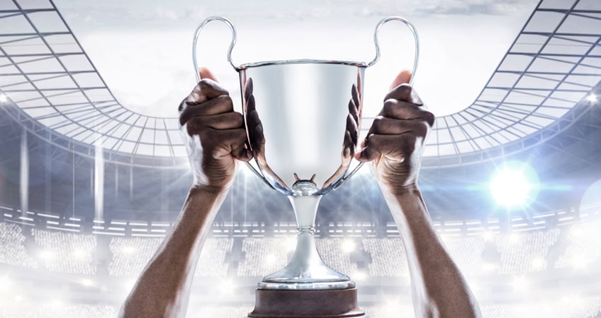 Hand holding a silver trophy cup at a sports stadium, symbolising achievement and success.