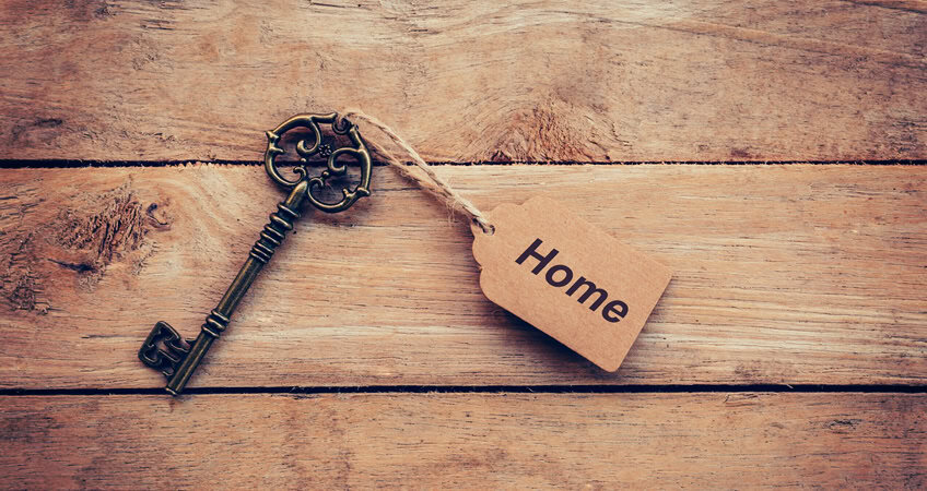 Old-fashioned brass key with "Home" tag on wooden background, symbolising safety for seniors.