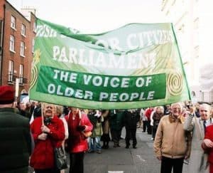 Elderly community holding a green banner at the Irish Senior Citizens Parliament.