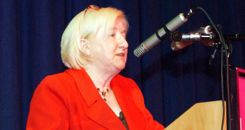 Alt text: Elderly woman speaking at podium during Irish Senior Citizens Parliament event.