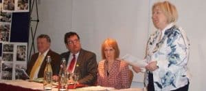 An elderly woman speaking at the Irish Senior Citizens Parliament discussing senior issues.
