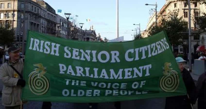 Accessible image showing Irish senior citizens holding a large green banner at a public event.