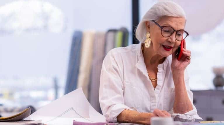 Elderly woman on phone at desk for Irish Senior Citizens Parliament.